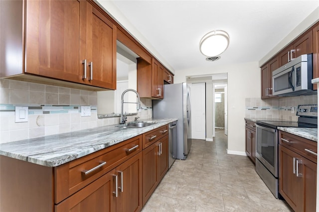 kitchen with light stone countertops, tasteful backsplash, light tile floors, sink, and appliances with stainless steel finishes