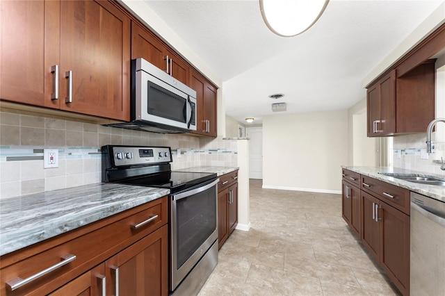 kitchen with appliances with stainless steel finishes, sink, tasteful backsplash, and light stone counters