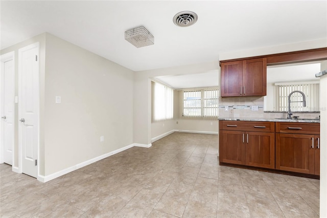 kitchen featuring backsplash, light stone counters, sink, and light tile floors