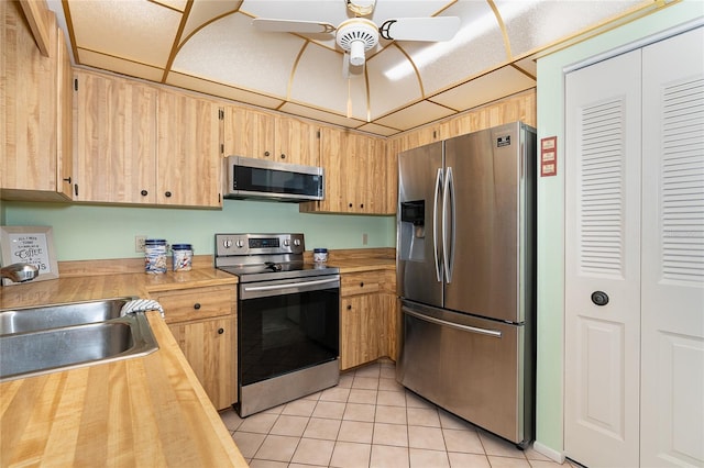 kitchen featuring ceiling fan, light tile floors, sink, appliances with stainless steel finishes, and wooden counters