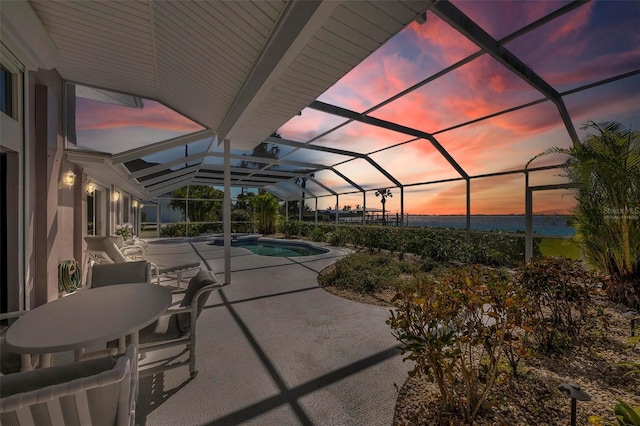 pool at dusk with glass enclosure and a patio area