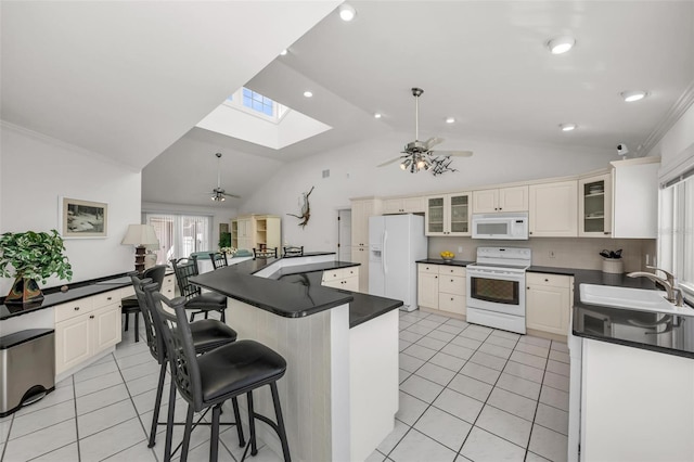 kitchen with a kitchen bar, vaulted ceiling with skylight, white appliances, sink, and a center island