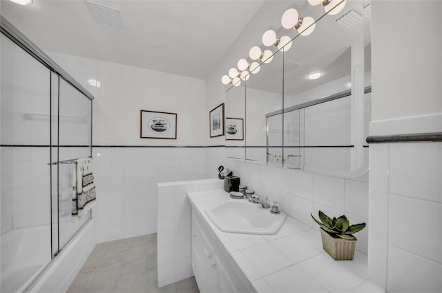 bathroom featuring tile patterned floors, shower / bath combination with glass door, vanity, and tile walls