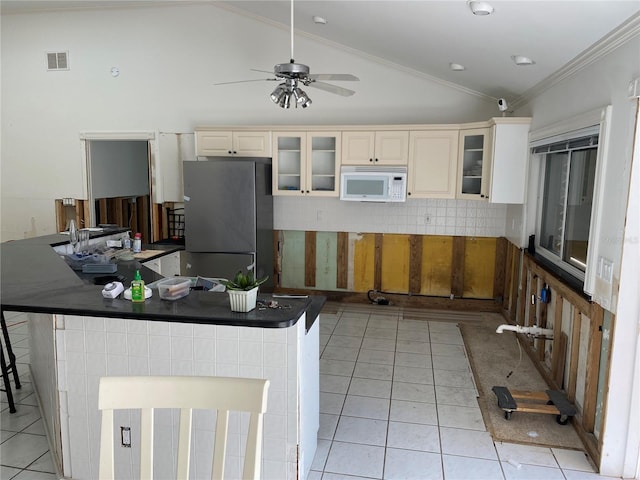 kitchen featuring stainless steel refrigerator, crown molding, vaulted ceiling, a kitchen bar, and light tile patterned flooring