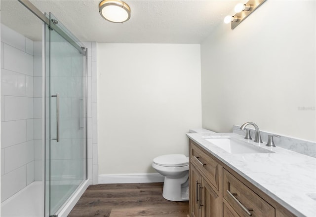 bathroom featuring toilet, a shower with shower door, a textured ceiling, vanity, and hardwood / wood-style floors