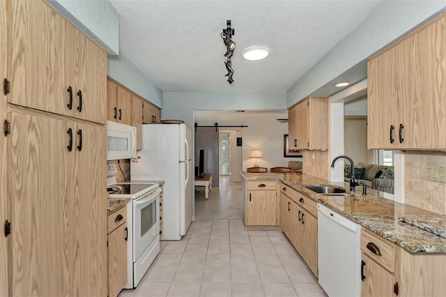 kitchen featuring kitchen peninsula, white appliances, sink, light stone counters, and a barn door