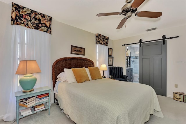 bedroom with a barn door, ceiling fan, ensuite bath, and light carpet