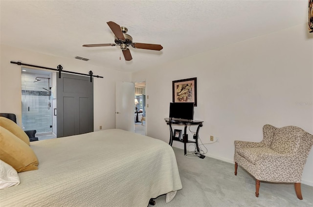 carpeted bedroom featuring a barn door, ensuite bath, and ceiling fan