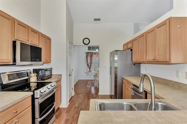 kitchen with a high ceiling, appliances with stainless steel finishes, sink, and light hardwood / wood-style flooring