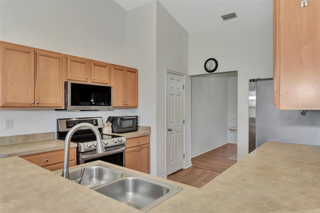 kitchen featuring high vaulted ceiling, light hardwood / wood-style flooring, and stainless steel appliances