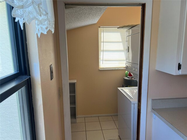 laundry room with stacked washer / dryer, light tile floors, and a textured ceiling