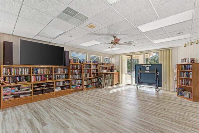 interior space with bookshelves, a drop ceiling, a ceiling fan, and wood finished floors