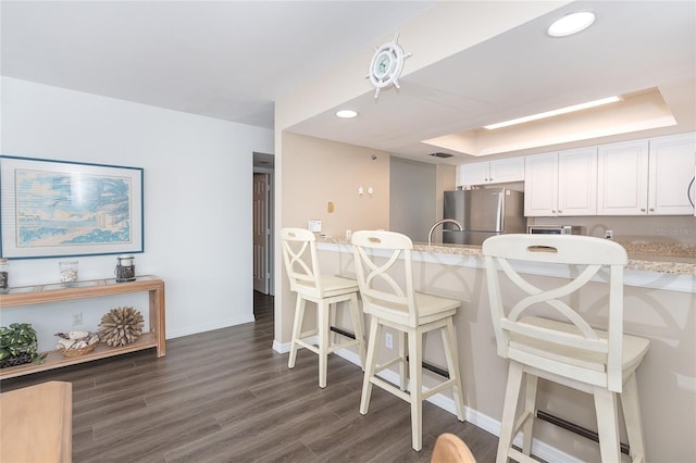 kitchen featuring white cabinets, a tray ceiling, dark wood-type flooring, and stainless steel refrigerator