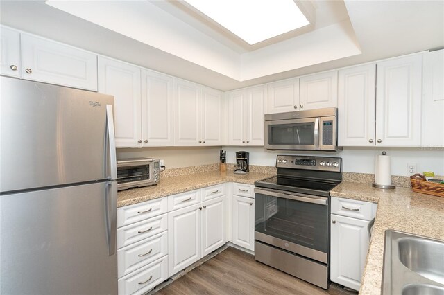 kitchen with appliances with stainless steel finishes, white cabinetry, and light hardwood / wood-style flooring