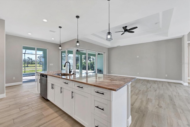 kitchen with a kitchen island with sink, sink, ceiling fan, a tray ceiling, and light stone counters