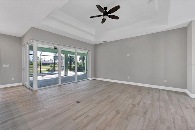 empty room with ceiling fan, light wood-type flooring, and a tray ceiling