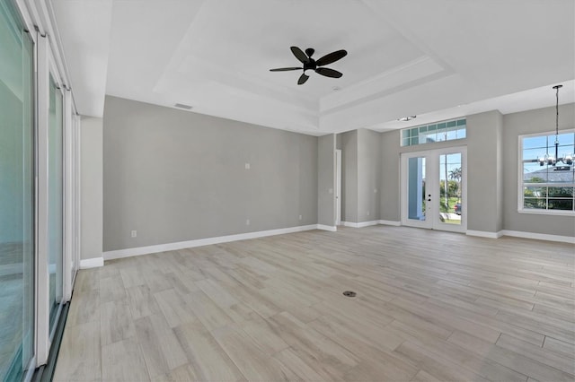 unfurnished room with ceiling fan with notable chandelier, light wood-type flooring, french doors, and a tray ceiling