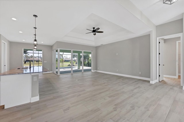 unfurnished living room with light hardwood / wood-style floors, a raised ceiling, ceiling fan, and sink