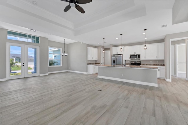 kitchen with white cabinets, stainless steel appliances, hanging light fixtures, and a tray ceiling