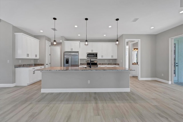 kitchen featuring a kitchen island with sink, hanging light fixtures, white cabinets, and stainless steel appliances