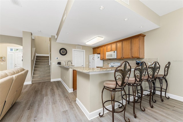 kitchen featuring kitchen peninsula, white appliances, light wood-type flooring, light stone counters, and a breakfast bar area