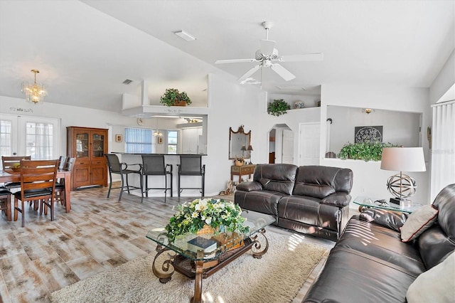 living room featuring ceiling fan with notable chandelier, vaulted ceiling, a wealth of natural light, and light hardwood / wood-style flooring