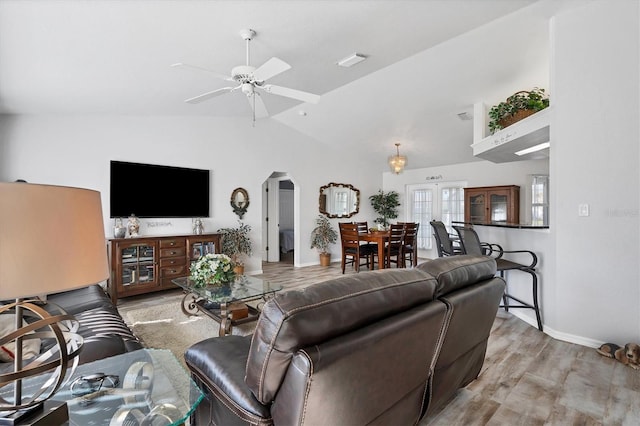 living room featuring ceiling fan with notable chandelier, vaulted ceiling, and light hardwood / wood-style flooring