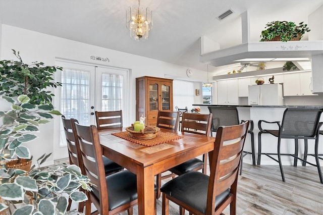 dining area featuring vaulted ceiling, light hardwood / wood-style flooring, french doors, and ceiling fan with notable chandelier