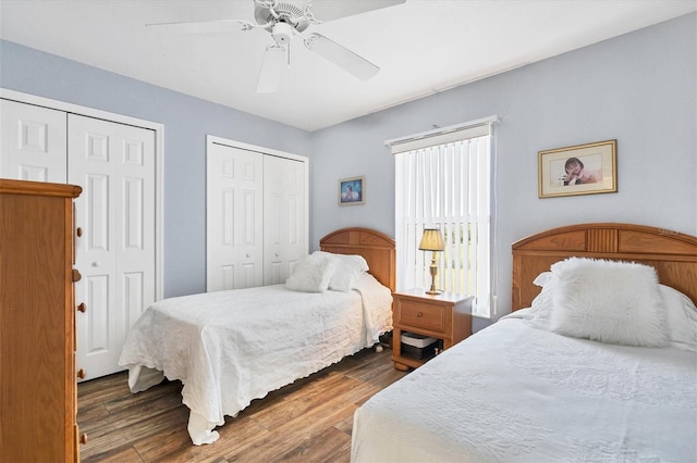 bedroom with ceiling fan, dark hardwood / wood-style flooring, and two closets