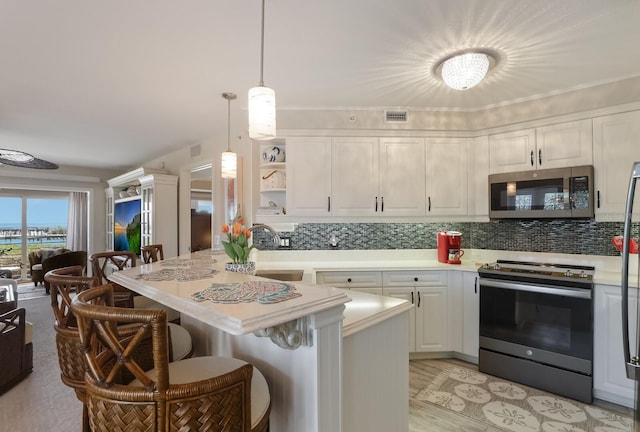 kitchen featuring hanging light fixtures, appliances with stainless steel finishes, a kitchen bar, white cabinets, and tasteful backsplash