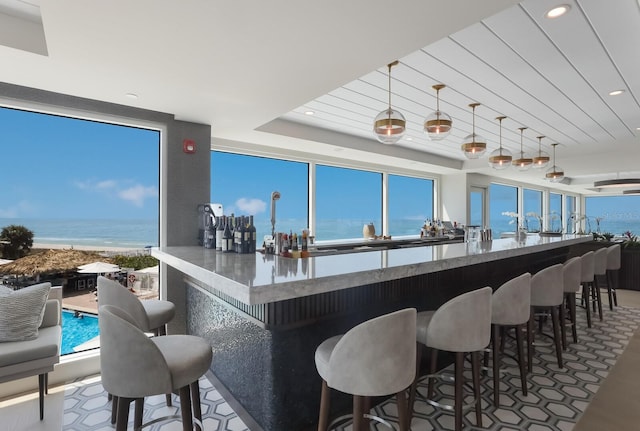 bar with a water view, hanging light fixtures, and a raised ceiling