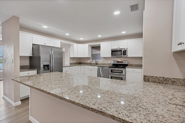 kitchen with appliances with stainless steel finishes, light stone counters, kitchen peninsula, light wood-type flooring, and white cabinetry