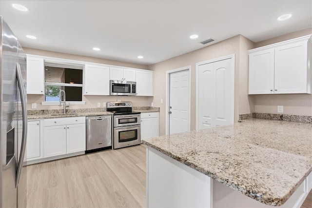 kitchen with light hardwood / wood-style flooring, stainless steel appliances, white cabinets, sink, and light stone counters