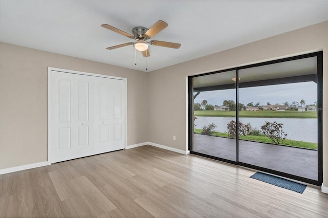 unfurnished bedroom with a closet, access to exterior, light hardwood / wood-style floors, a water view, and ceiling fan