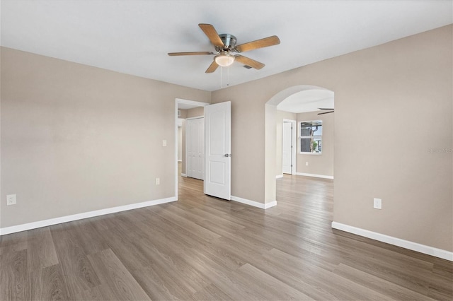 empty room featuring arched walkways, baseboards, ceiling fan, and light wood finished floors