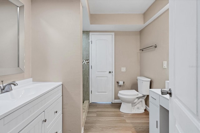 bathroom featuring toilet, wood finished floors, vanity, baseboards, and tiled shower