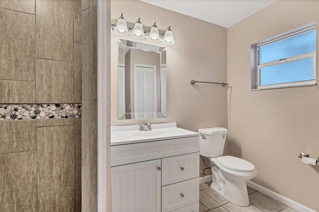 bathroom featuring tile patterned flooring, toilet, vanity, baseboards, and a tile shower