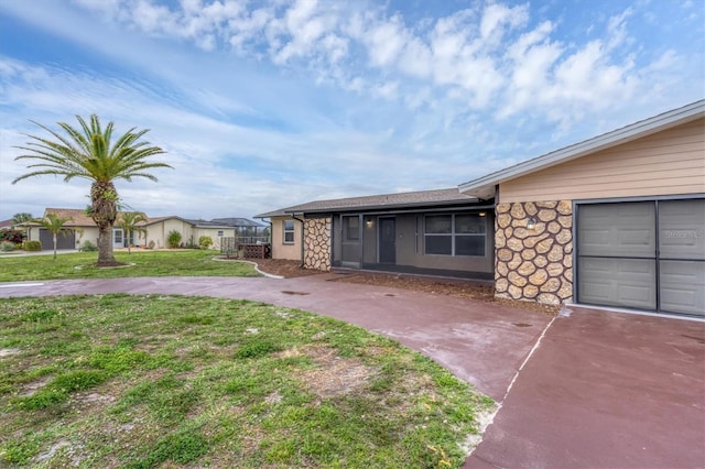 exterior space featuring an attached garage, stone siding, a front yard, and driveway