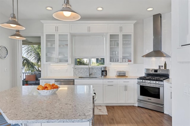 kitchen with white cabinets, appliances with stainless steel finishes, light hardwood / wood-style flooring, backsplash, and wall chimney exhaust hood