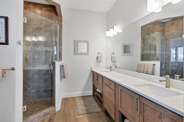 bathroom featuring a shower with door, oversized vanity, dual sinks, and wood-type flooring