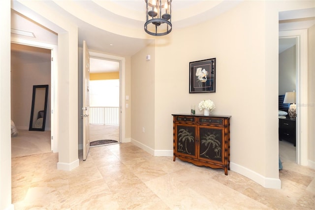 hall featuring light tile floors, a chandelier, and a tray ceiling