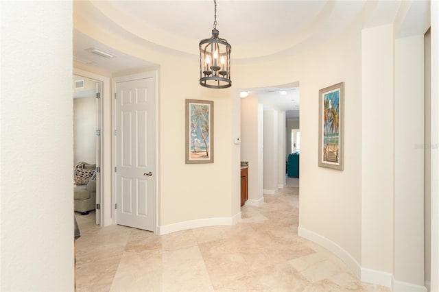 hallway featuring a notable chandelier, a raised ceiling, and light tile flooring