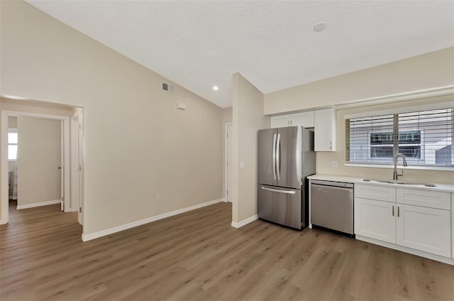 kitchen with light hardwood / wood-style flooring, white cabinetry, appliances with stainless steel finishes, lofted ceiling, and sink