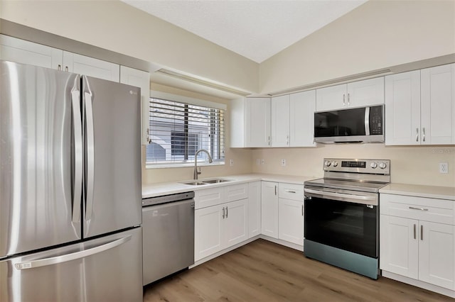 kitchen with lofted ceiling, white cabinetry, dark wood-type flooring, appliances with stainless steel finishes, and sink