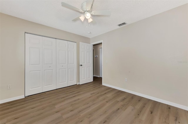 unfurnished bedroom featuring a textured ceiling, a closet, ceiling fan, and light wood-type flooring