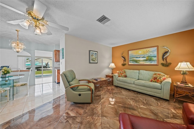 tiled living room featuring a textured ceiling and ceiling fan with notable chandelier