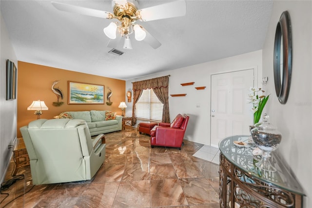 living room featuring ceiling fan, a textured ceiling, and dark tile flooring