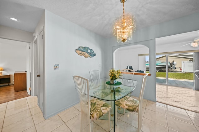 tiled dining space featuring a textured ceiling and ceiling fan with notable chandelier