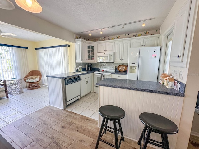 kitchen featuring a kitchen bar, white cabinets, white appliances, and kitchen peninsula