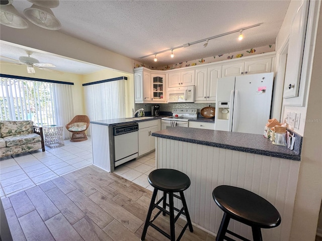 kitchen with white cabinetry, a breakfast bar, white appliances, and kitchen peninsula